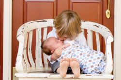Bild: ein kleines Kind hält ein Baby im Arm und sitzt auf einer Bank